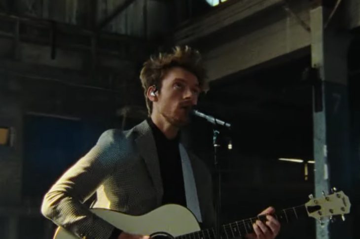 FINNEAS wearing a suit playing an acoustic guitar