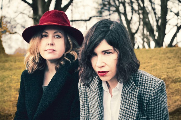 Photo of Sleater Kinney's Corrin Tucker & Carrie Brownstein outside in front of trees.