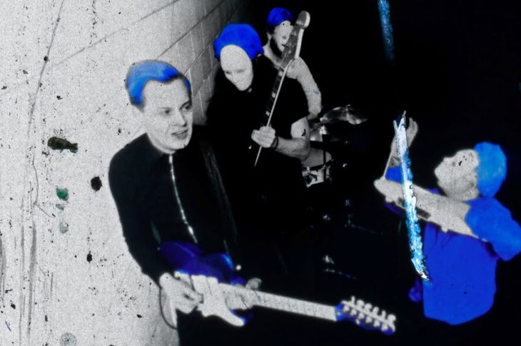 black, white, and blue photo of Jack White and masked musicians performing in a concrete hallway.